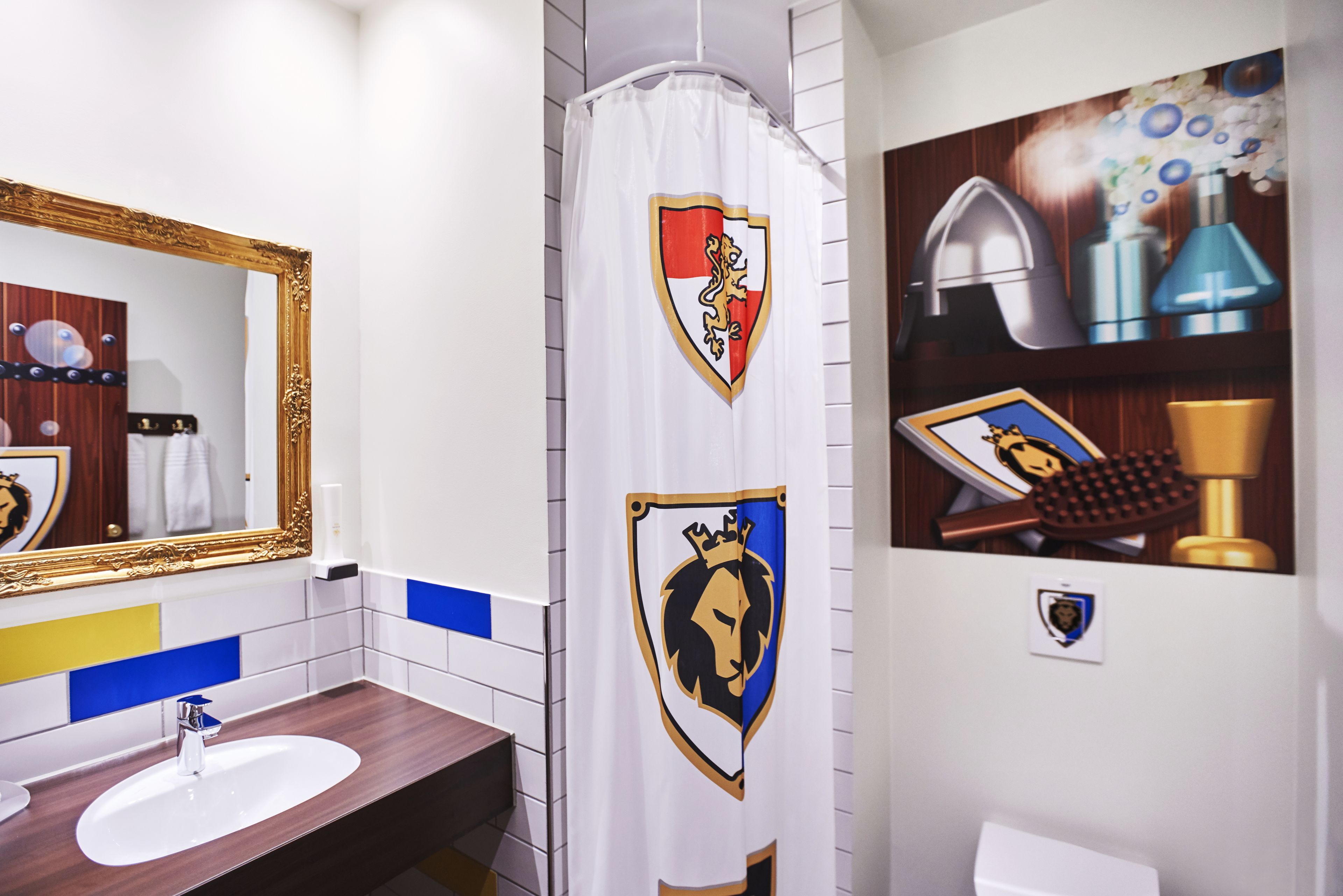 A bathroom with a white sink, a mirror with a gold frame, and a shower curtain with a lion emblem.