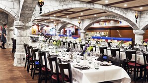 Un restaurant doté d’arches en pierre et de poutres en bois, avec des tables recouvertes de nappes blanches et des chaises rouges.