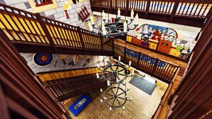 L’intérieur d’un hôtel à plusieurs niveaux, avec un lustre central, des rampes en bois et une zone recouverte d’une moquette bleue.