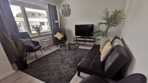 A modern living room with a sofa, chairs, a coffee table, a TV, and a potted plant. - Haave Apartments (Valkeakoski)