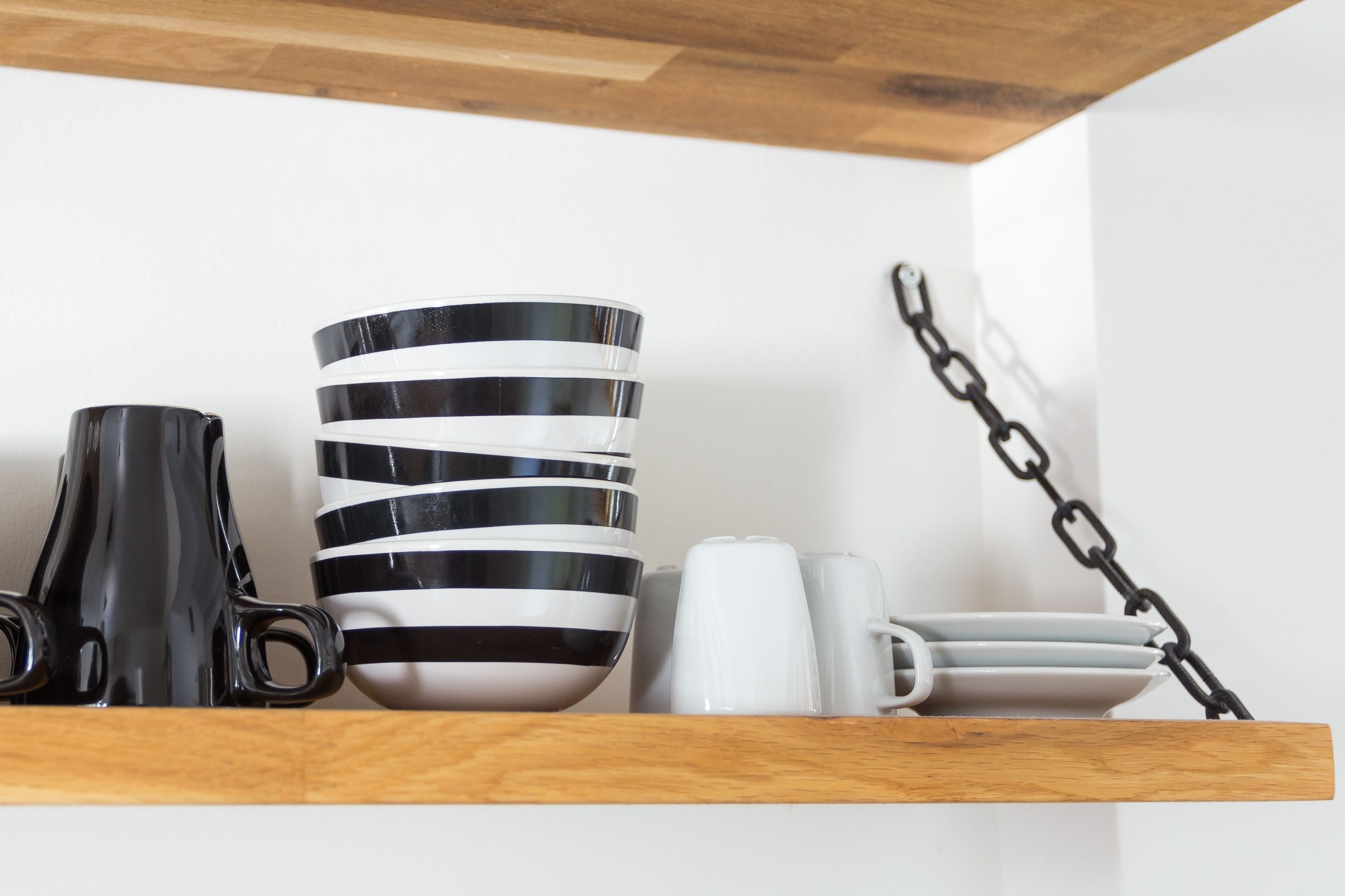Una repisa de madera con tazas a rayas negras y blancas, una taza negra y tazas blancas.