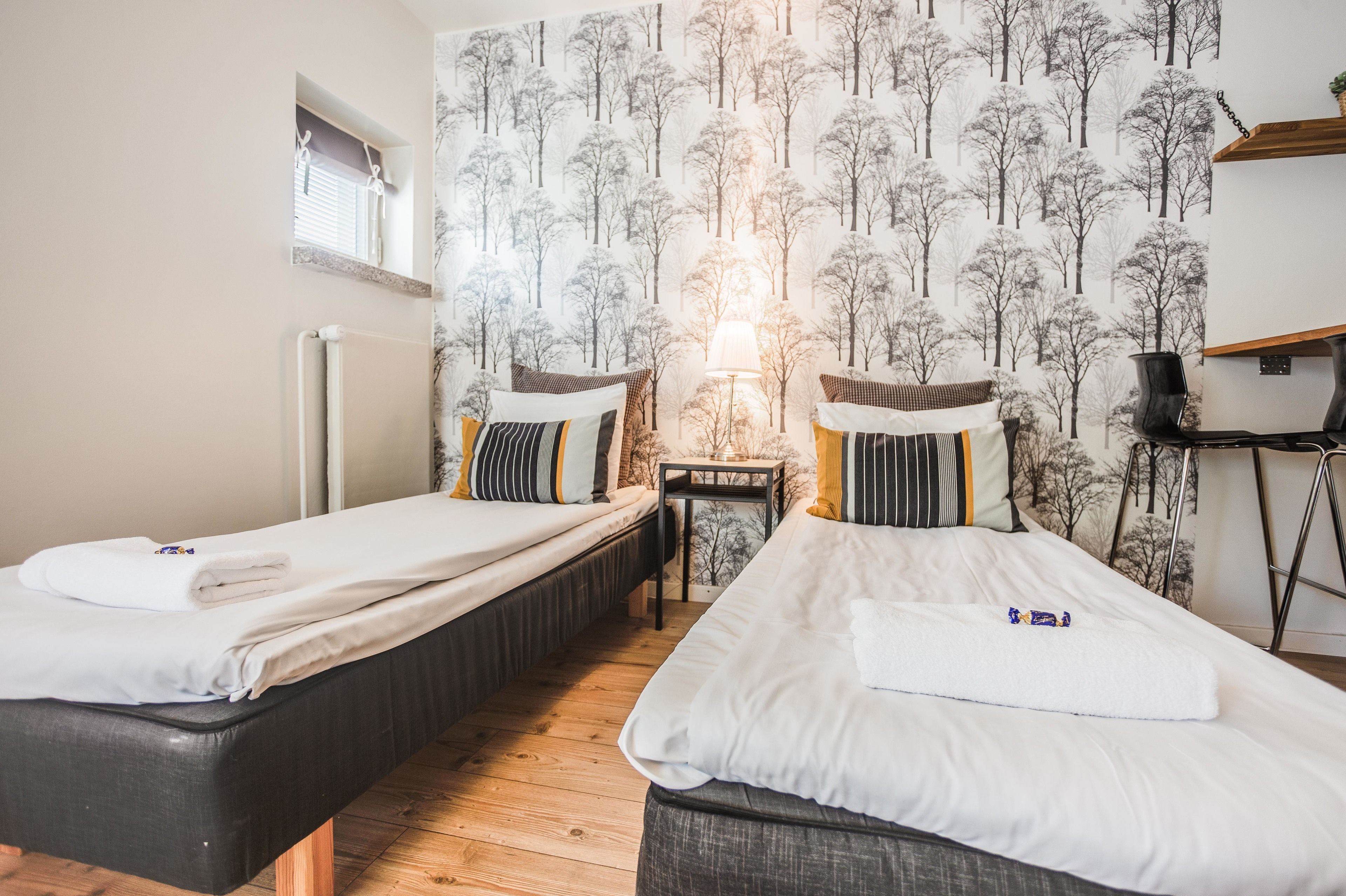 A room with two beds, a small table, a lamp, and a window.