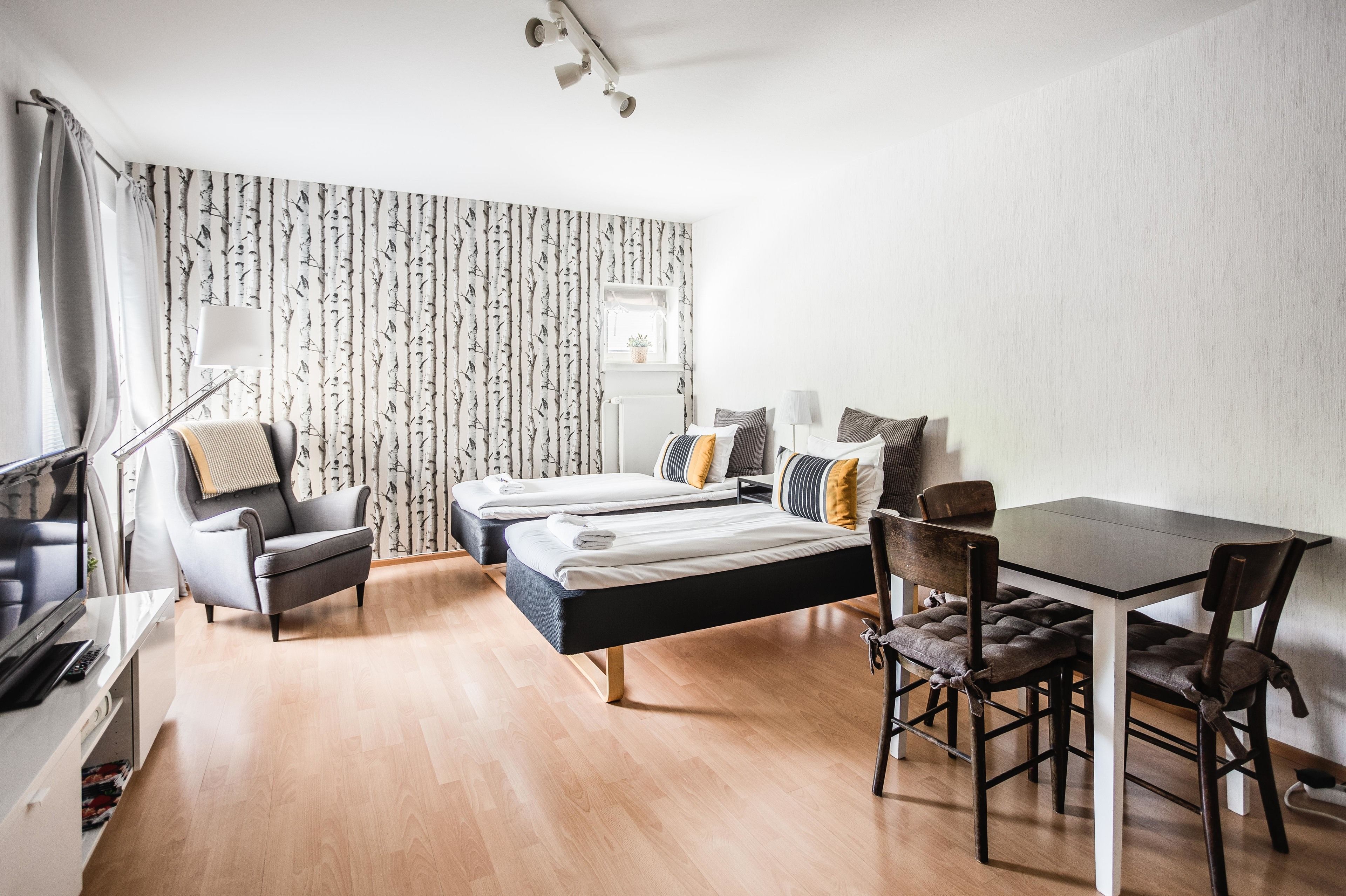 A modern hotel room with two single beds, a dining table, and a TV.