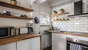 A modern kitchen with white cabinets, wooden countertops, a microwave, a coffee maker, and a stove. - Haave Apartments (Valkeakoski)