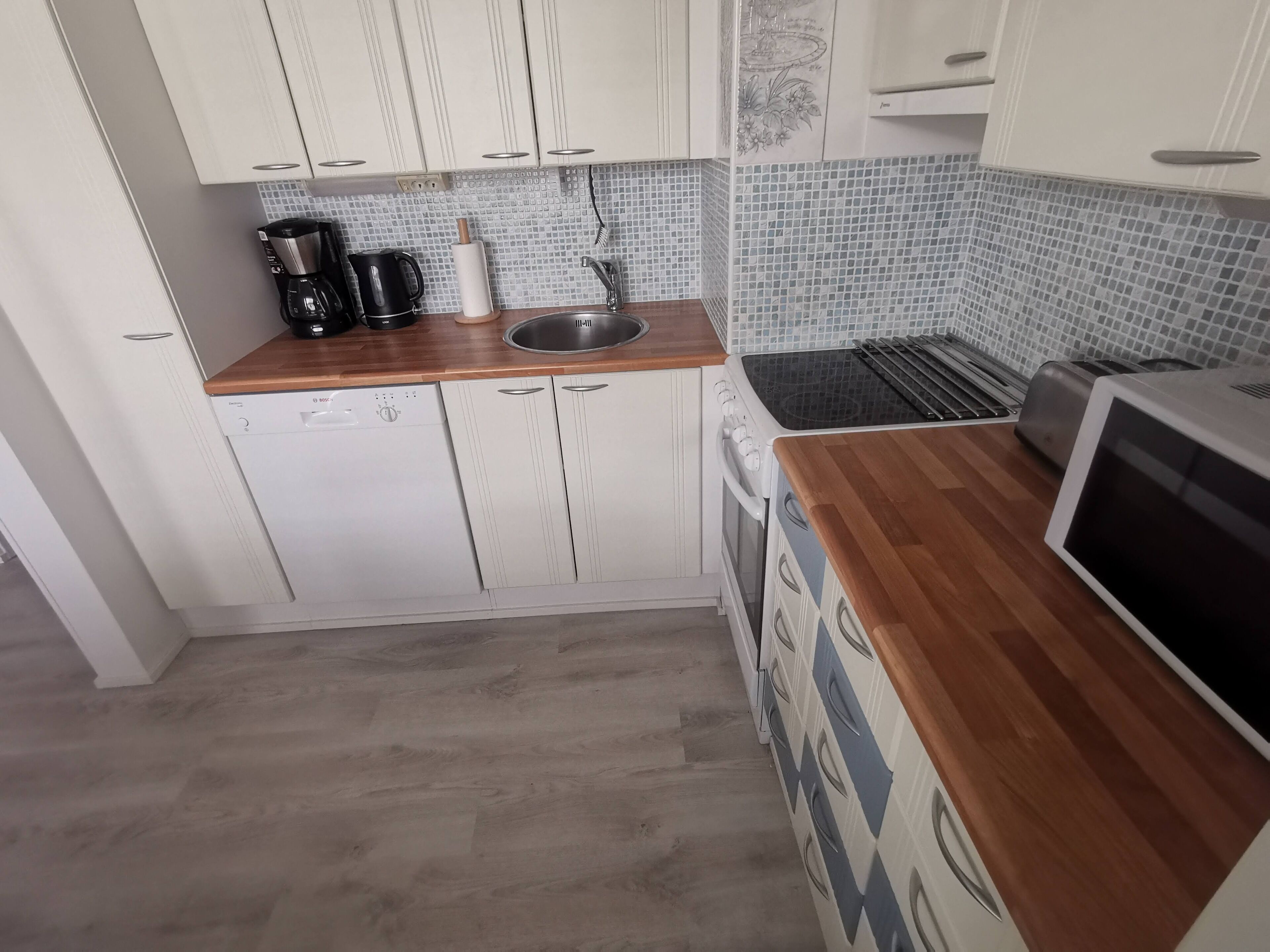 A compact kitchen with white cabinets, a wooden countertop, a built-in oven, a toaster, and a microwave.