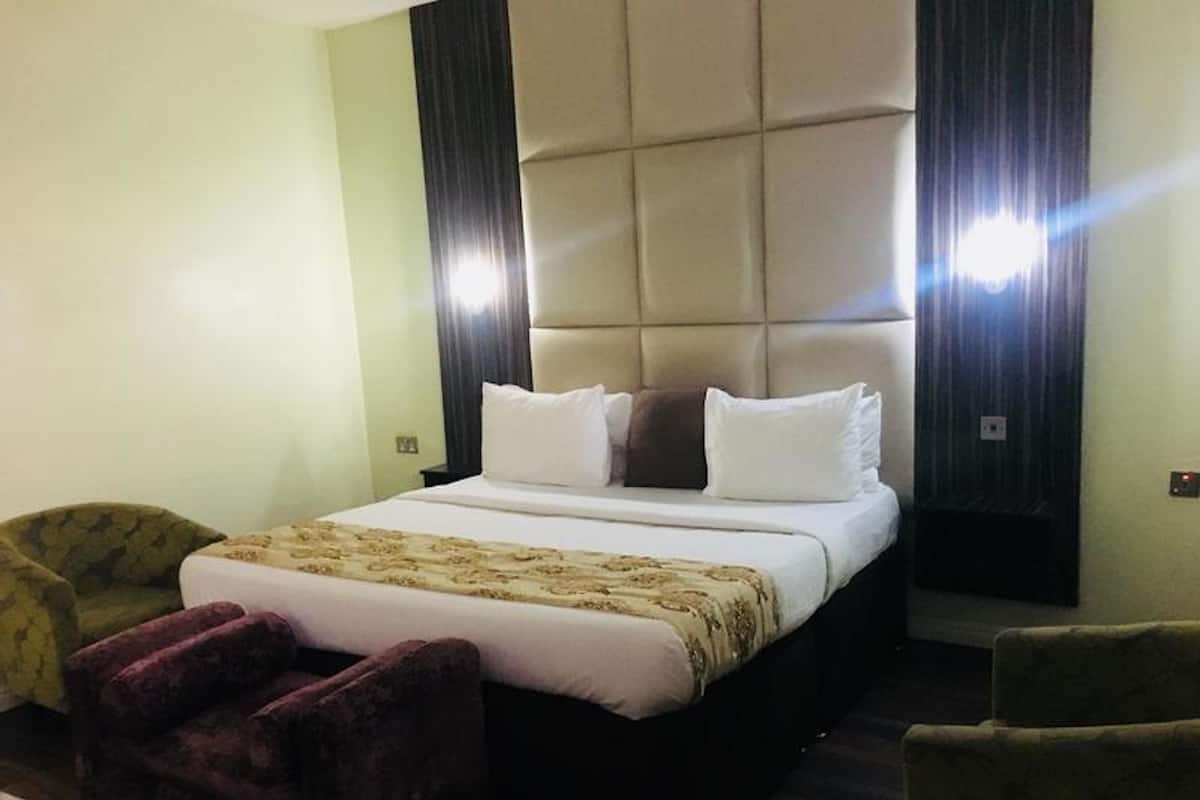 Een hotelkamer met een groot bed, twee fauteuils, een decoratieve plaid en een donker hoofdbord.