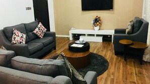 Ein modernes Wohnzimmer mit grauem Sofa, einem kleinen Sessel, einem Couchtisch und einem an der Wand befestigten Fernseher.
