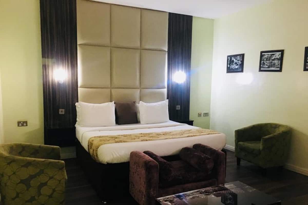 Een hotelkamer met een groot bed, twee fauteuils, een klein tafeltje en een muur met ingelijste foto's.