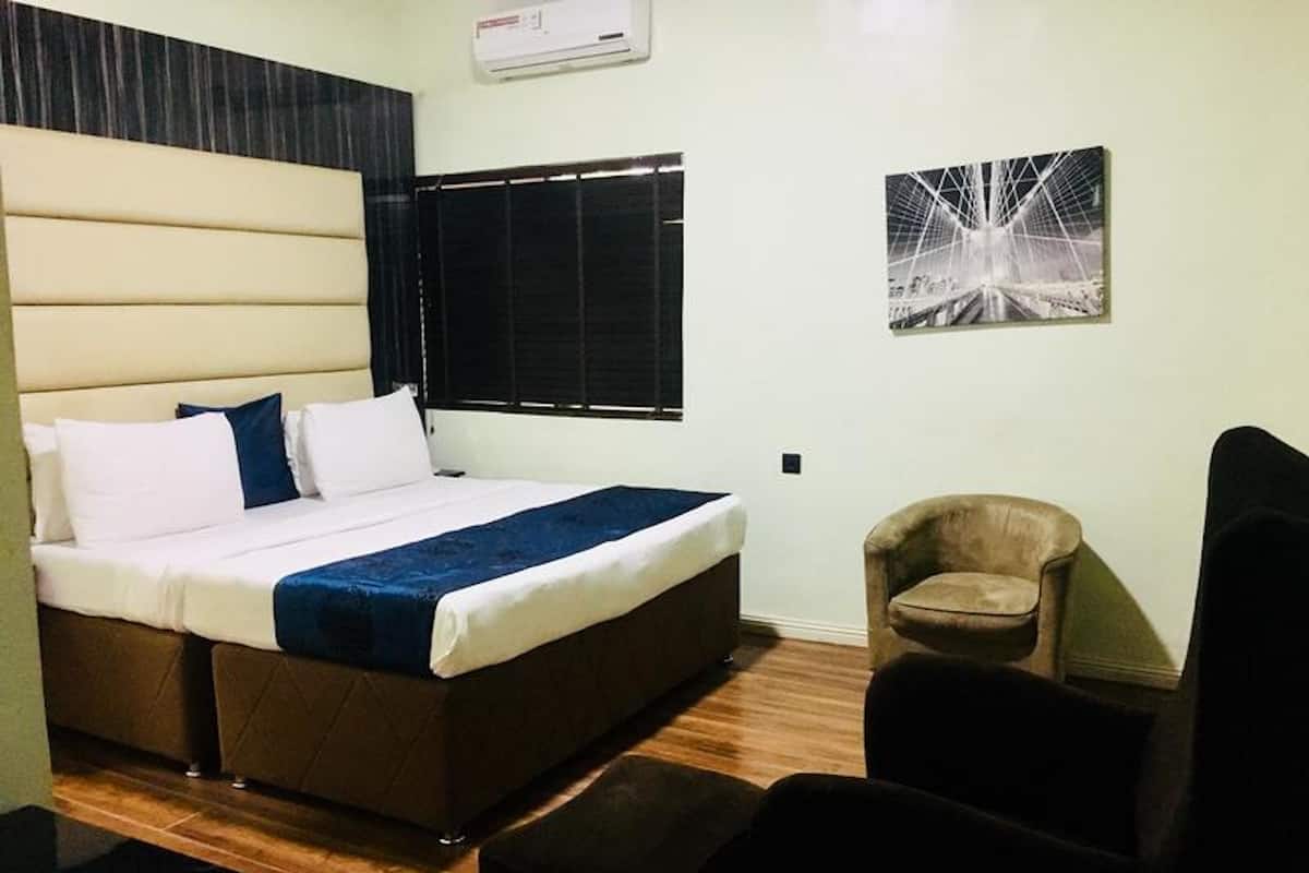 Een hotelkamer met een bed, een stoel, een klein tafeltje, een raam met zonwering en een wandairconditioner.