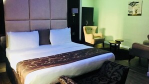 Ein Hotelzimmer mit einem großen Bett, einem Sessel, einem kleinen Tisch und einem Wandbild.