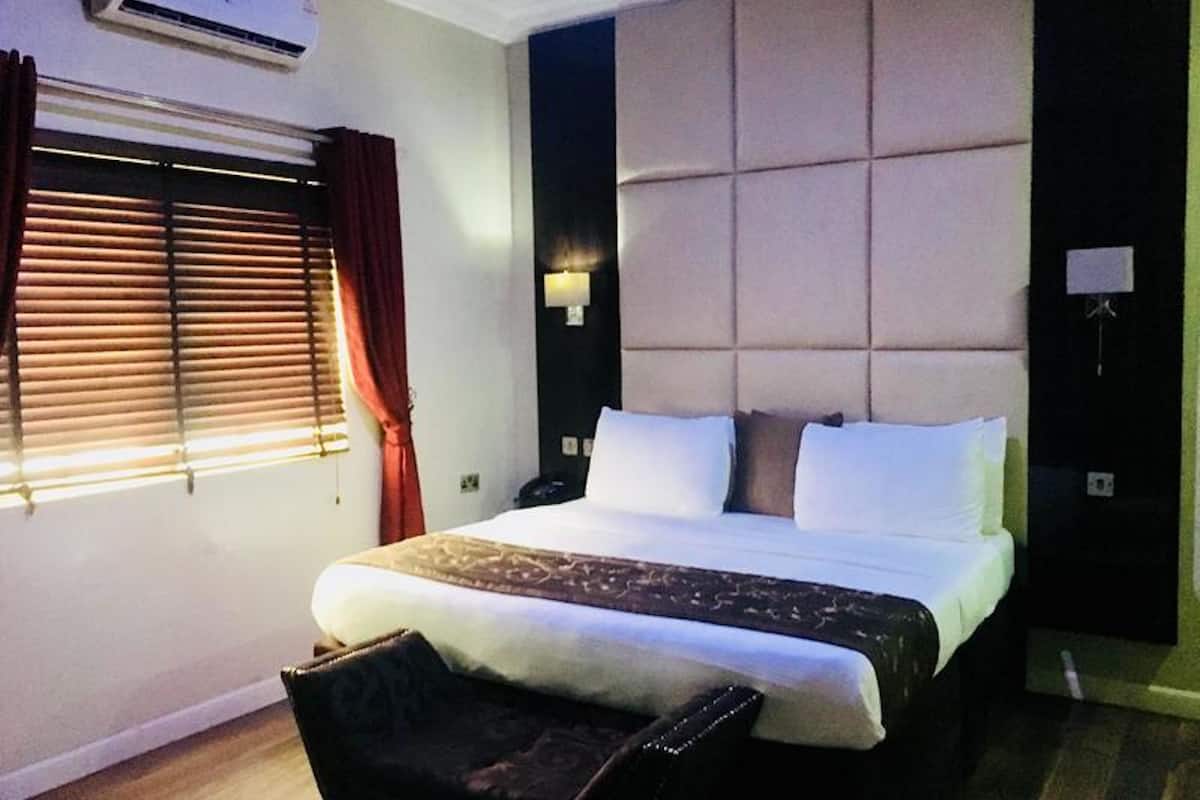 Hotelkamer met een bed, een stoel, een raam met zonwering, een airconditioning en een wandlamp.
