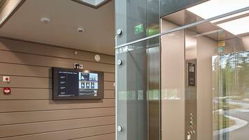 An elevator with a glass door, a digital information board, and a beige wall with horizontal lines.