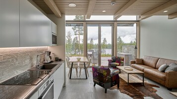 Cozinha moderna com uma ilha grande, área de refeições com mesa e cadeiras, e um espaço de estar aconchegante com sofá e poltrona estampada.