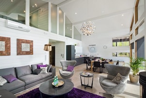 Uma sala de estar ampla, com sofá, poltronas, mesa de centro e área de jantar com mesa e cadeiras.