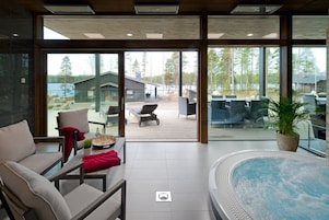 Interior moderno com uma grande porta de vidro que dá para um deck externo, uma banheira de hidromassagem e uma área de estar com vista para a paisagem ao redor.
