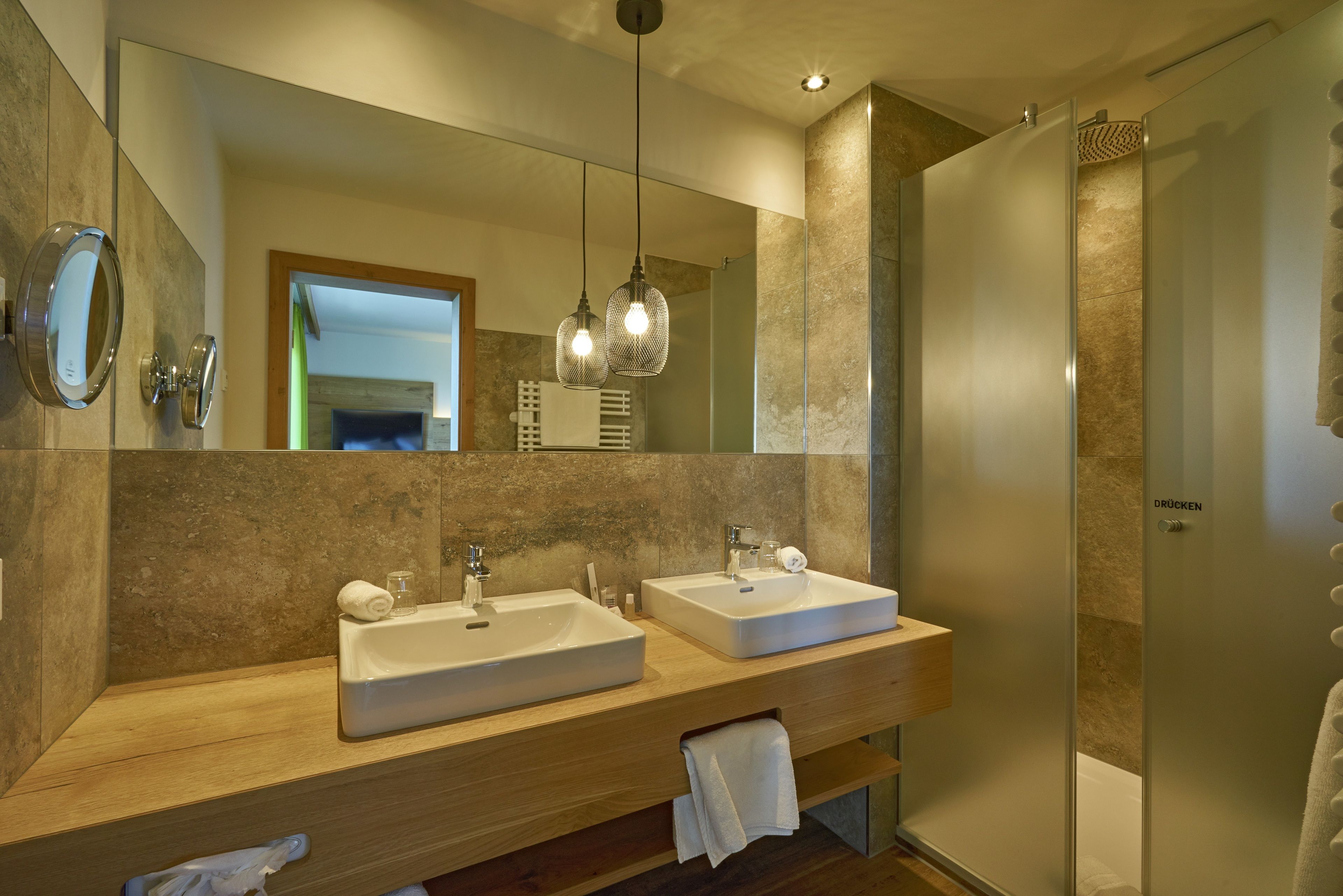 A modern bathroom with two sinks, a large mirror, and a shower area.