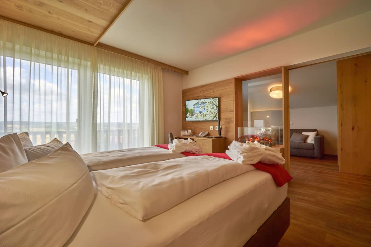 A hotel room with two beds, a TV, a wooden ceiling, and a balcony view.