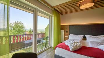 Quarto de hotel com uma grande porta de vidro deslizante que dá para uma varanda, cama com roupa de cama branca e vermelha, e teto de madeira.