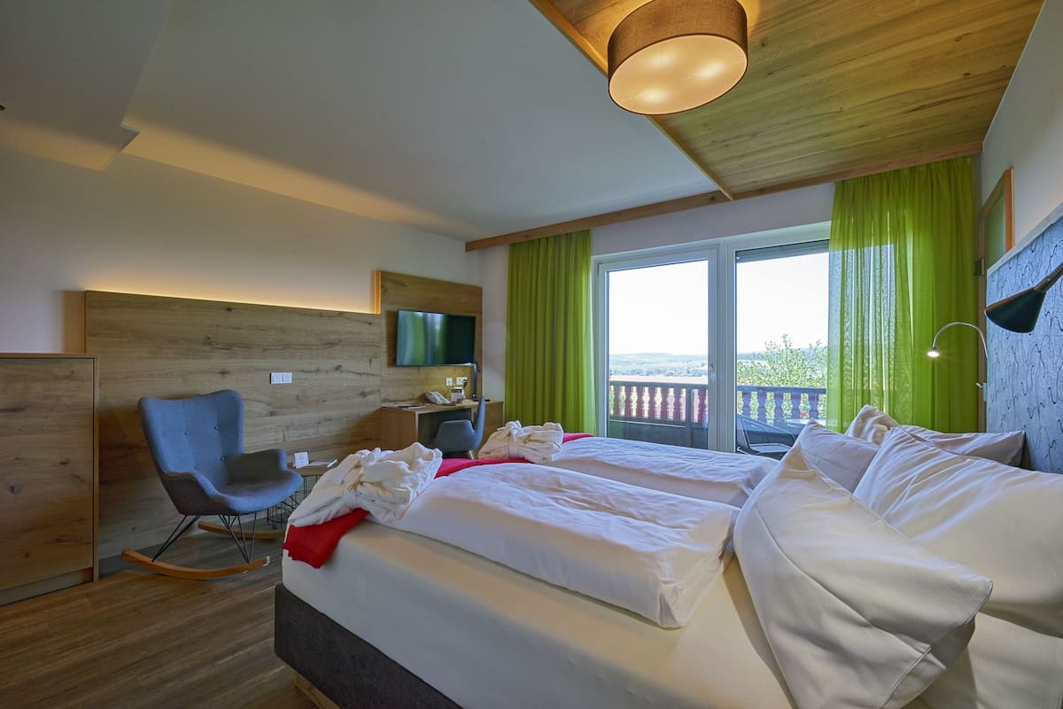 A hotel room with a bed, a desk, a chair, a TV, and a balcony with green curtains.