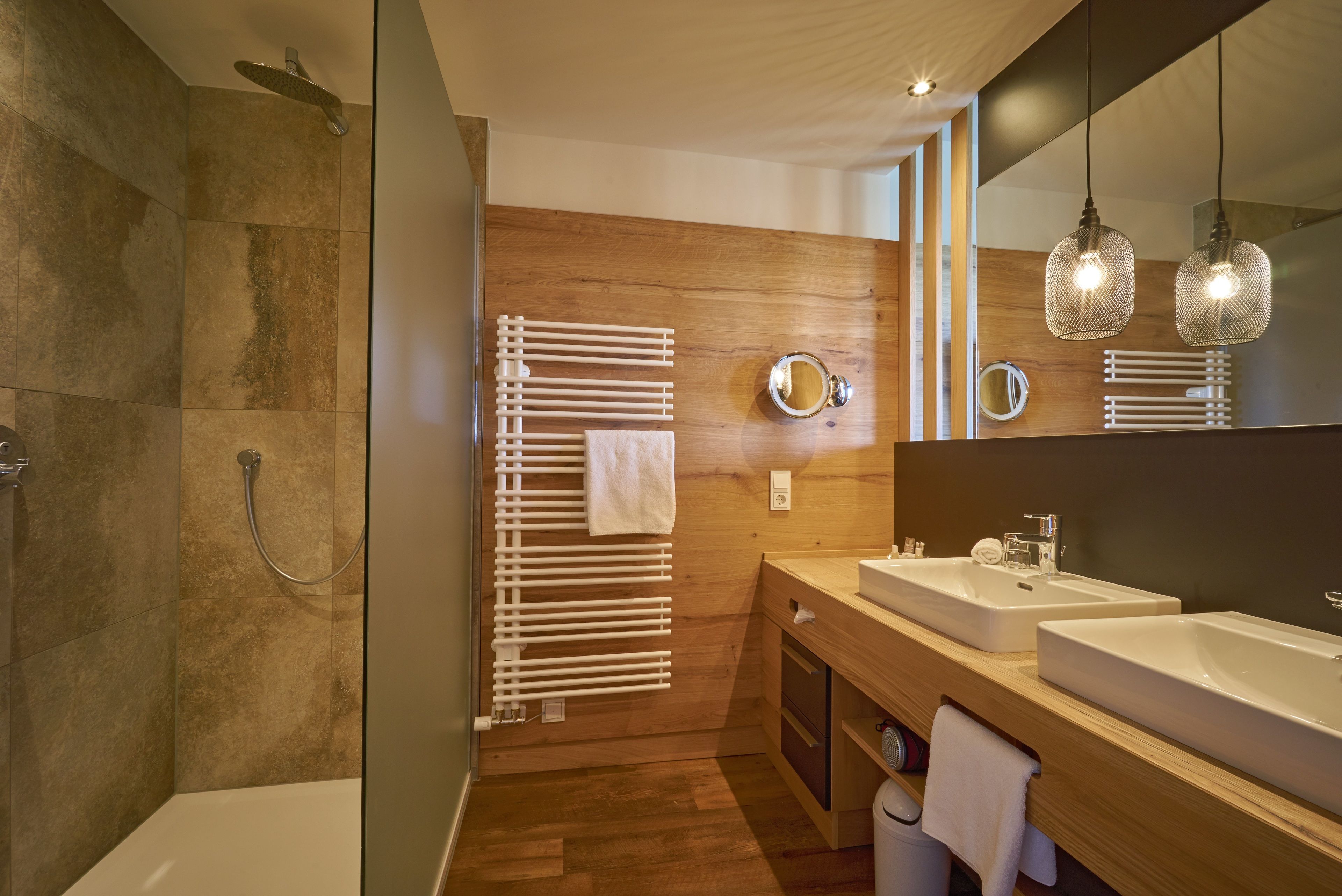 Une salle de bain moderne avec un meuble-lavabo en bois, deux vasques, un grand miroir et un espace douche.