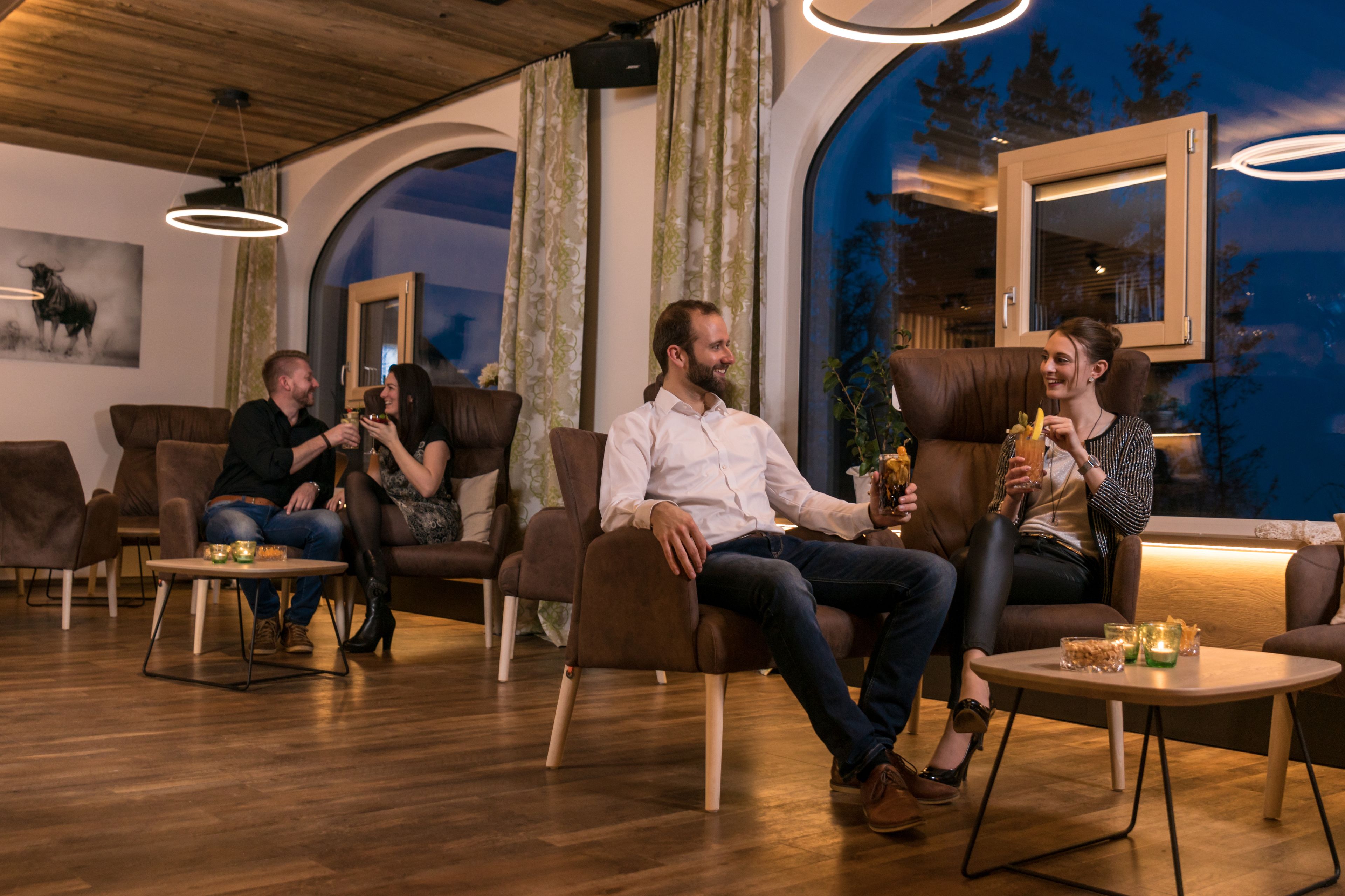 Et moderne interiør med lædersofaer, træborde og et stort vindue med udsigt til træer.