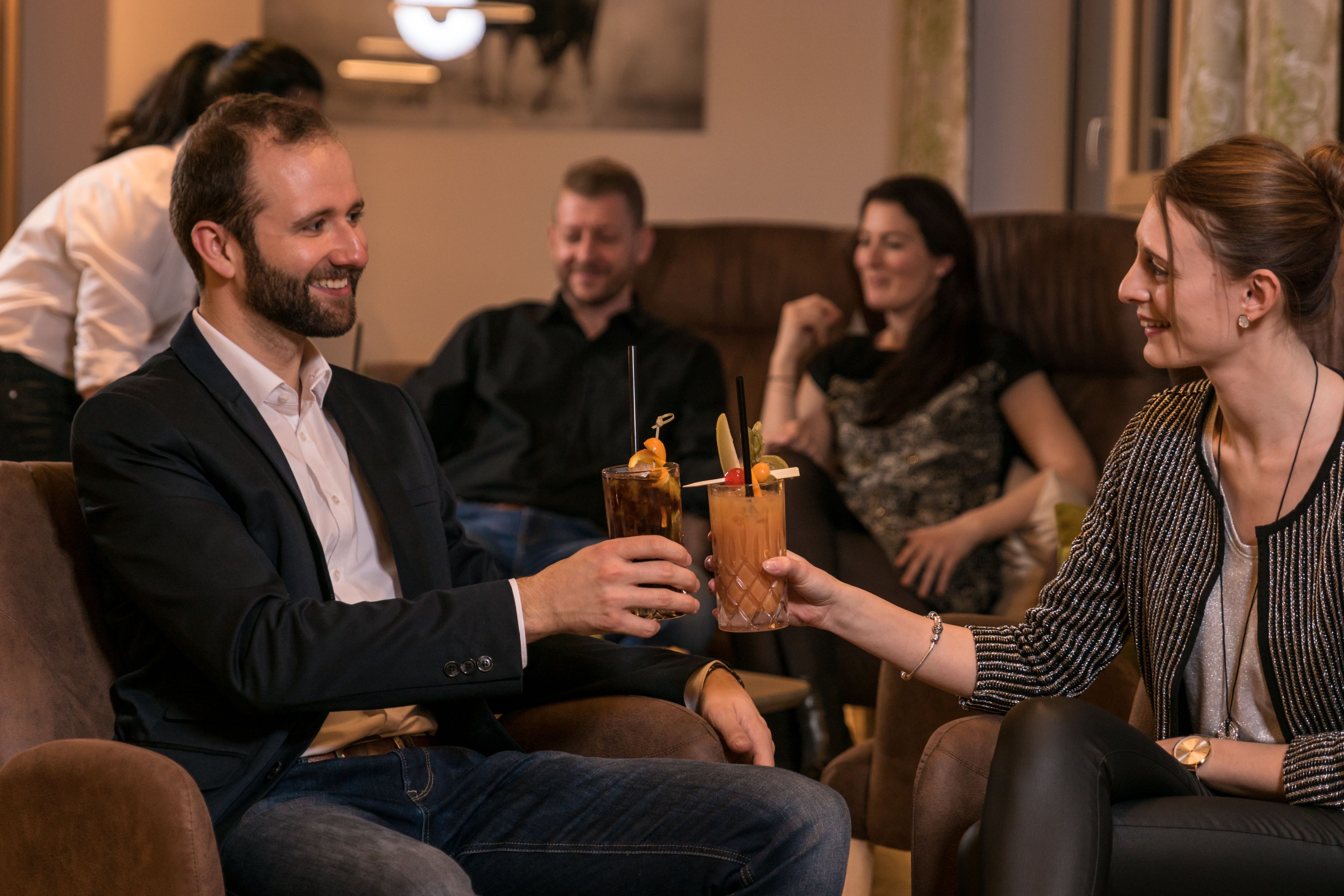A group of people seated on a couch in a room with a modern interior design, holding drinks.