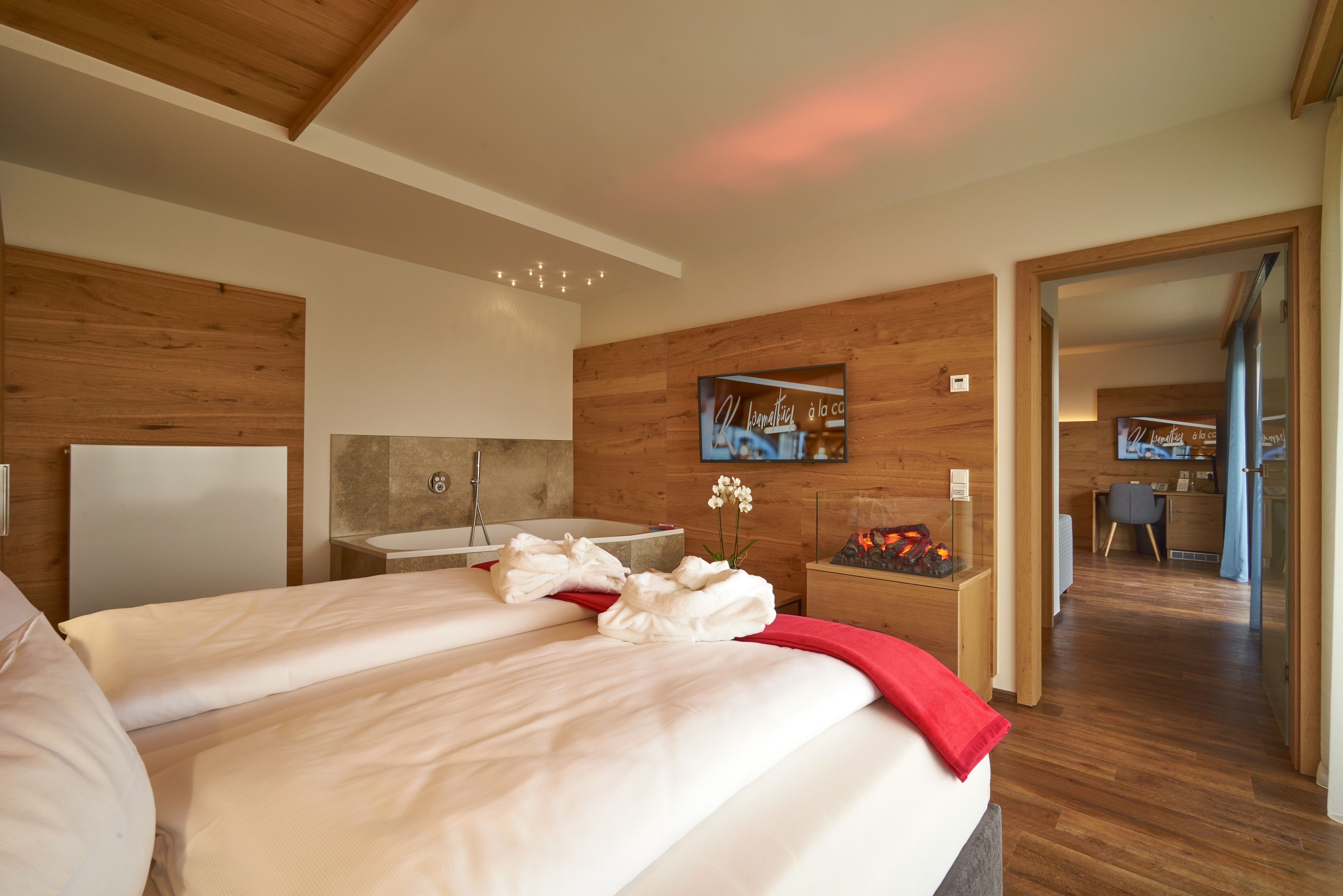 Una habitación de hotel moderna con una cama grande, paneles de madera, un baño con bañera y un escritorio pequeño con silla.