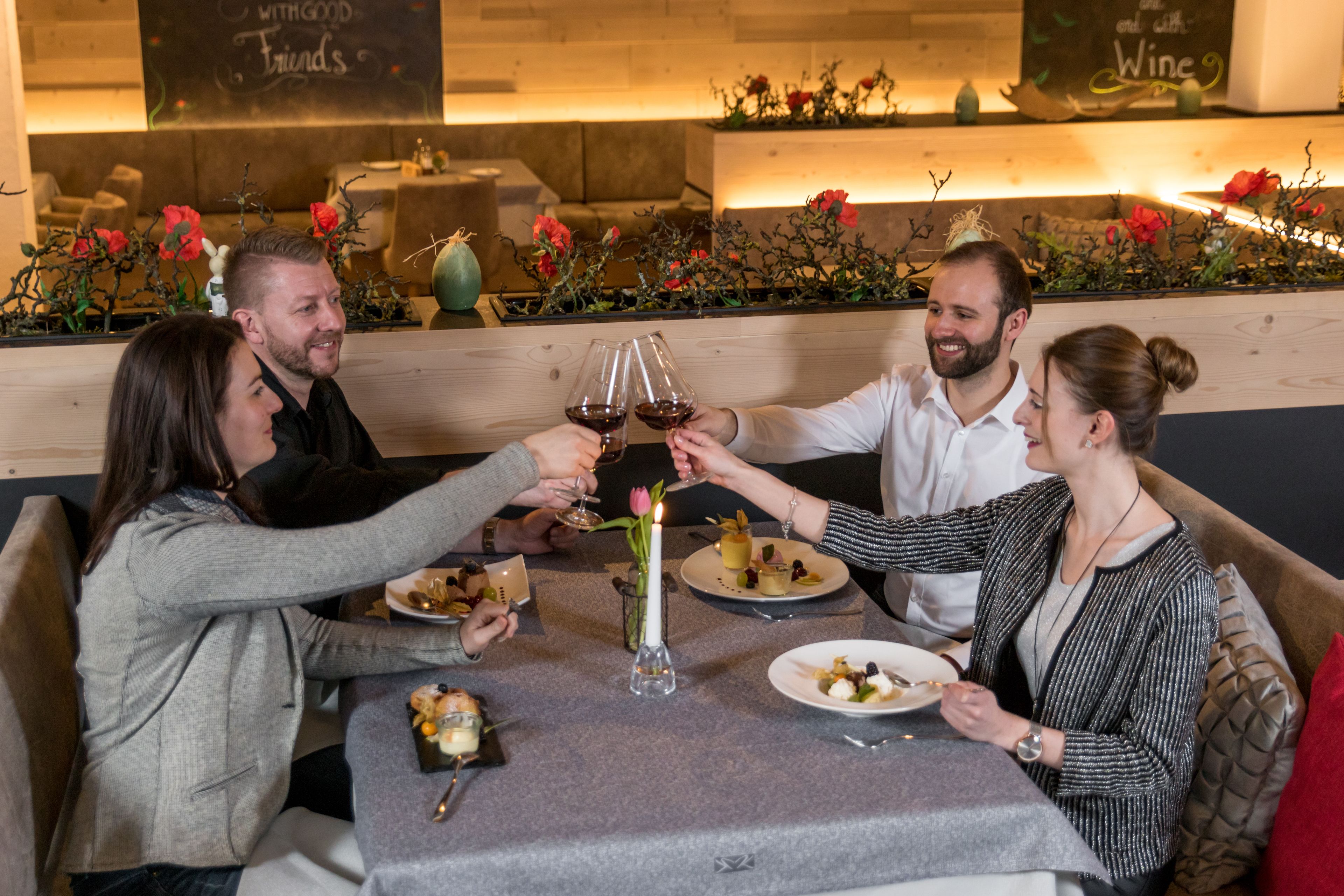 A group of people toasting with wine glasses at a restaurant with a wooden interior and floral decorations.