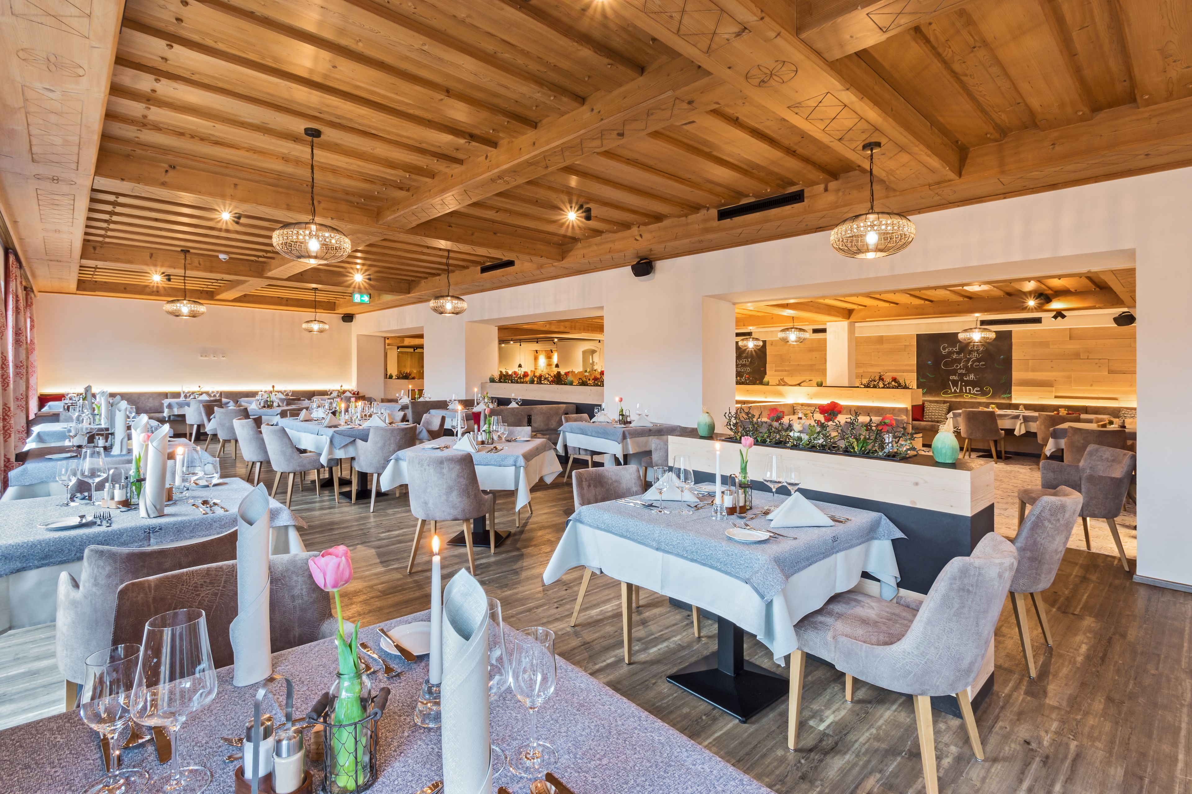 A restaurant with multiple dining tables, wooden ceiling beams, and pendant lighting.