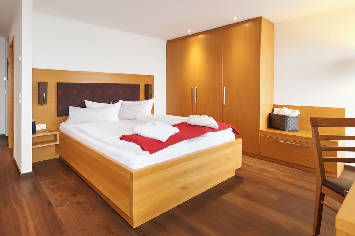 A modern hotel room with a wooden bed, a wardrobe, a desk, and a chair.
