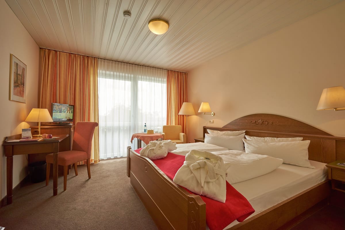 A hotel room with a wooden bed, two bedside lamps, a desk with a chair, a small table, and a television.