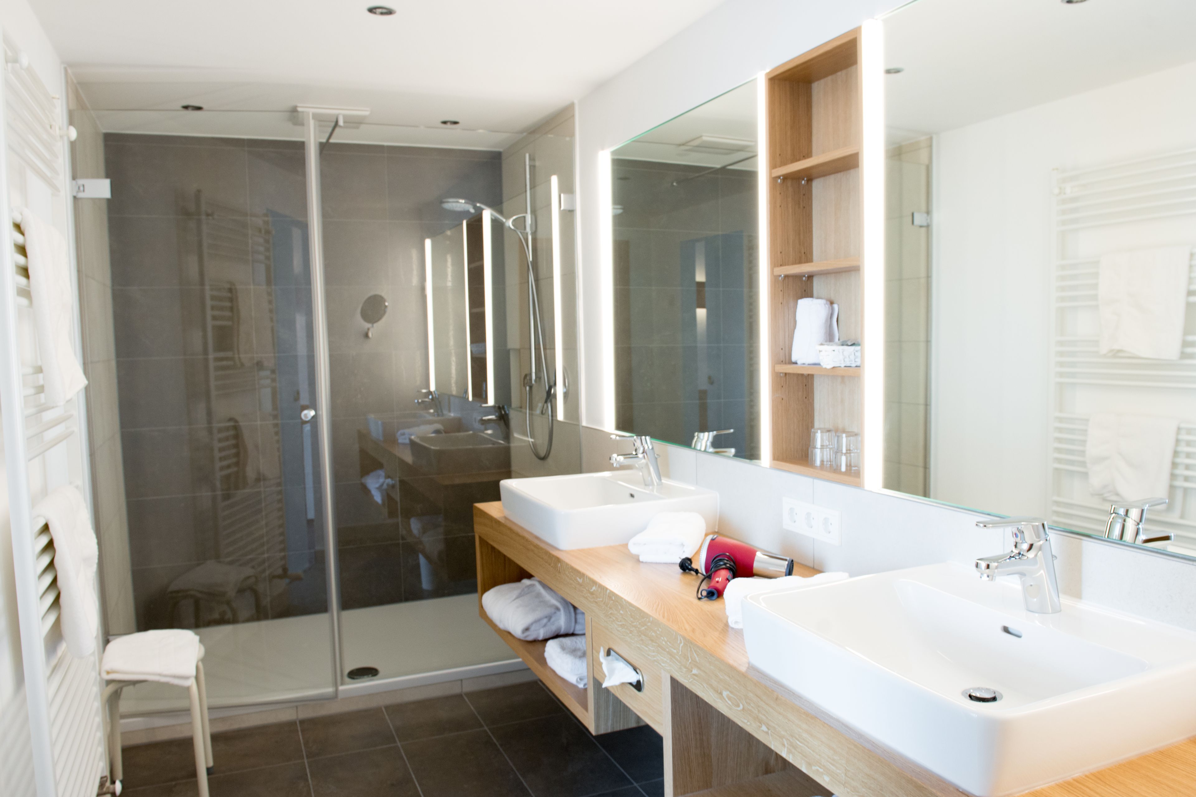 Een moderne badkamer met twee wastafels, een douchecabine van glas en een grote spiegel.