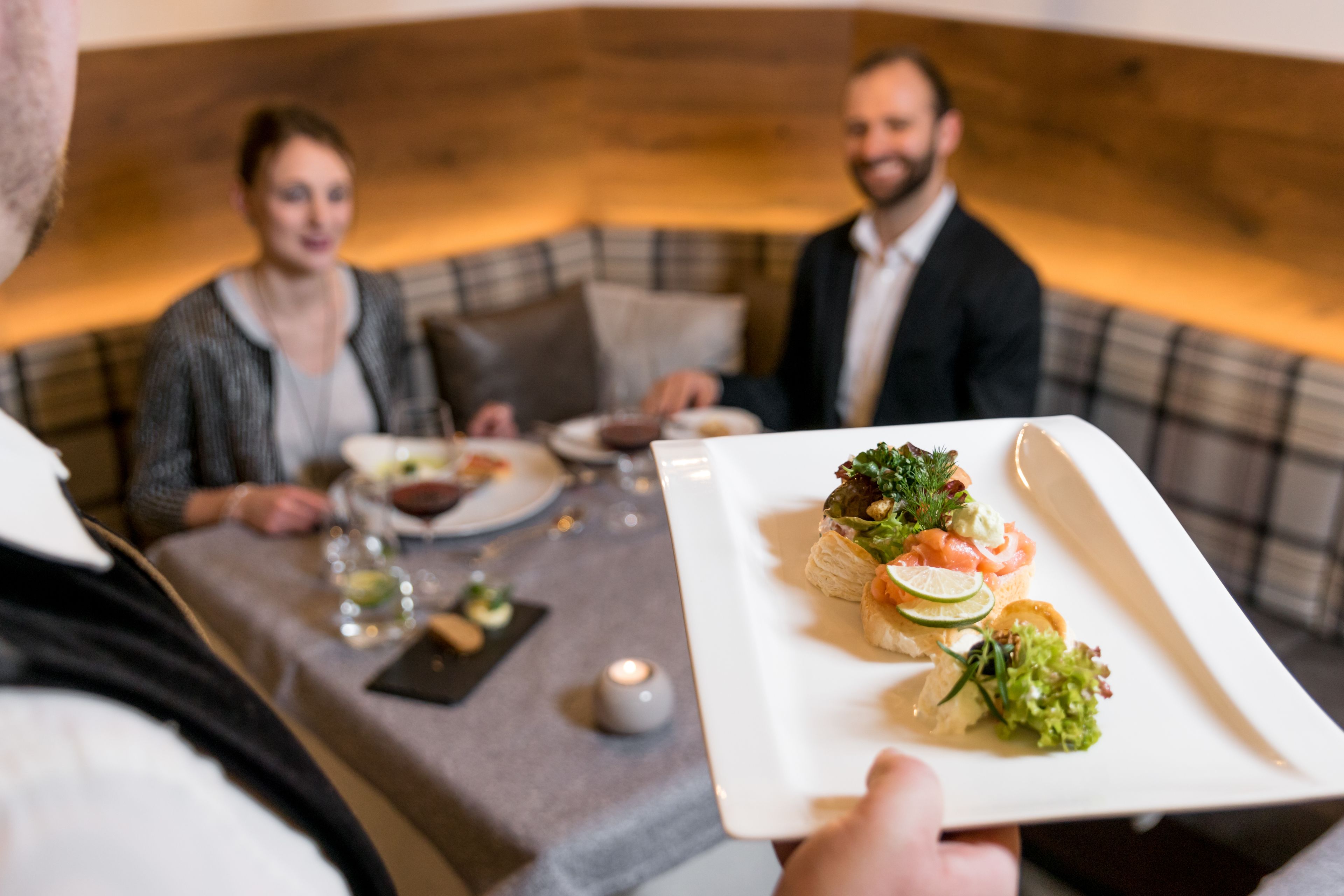 Una mesa de comedor con un plato blanco de aperitivos, una vela y una botella de vino.
