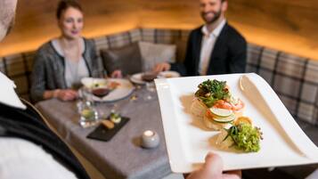 Una mesa de comedor con un plato blanco de aperitivos, una vela y una botella de vino.