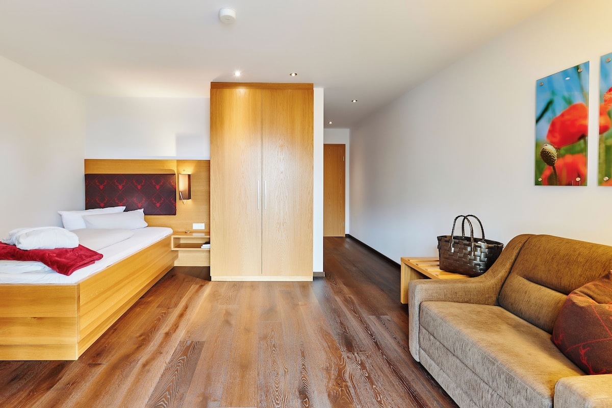 A modern hotel room with a wooden bed, a sofa, and a wooden partition.