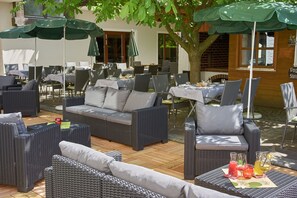 Un área de estar al aire libre con mobiliario de mimbre, sombrillas verdes y una mesa con bebidas.