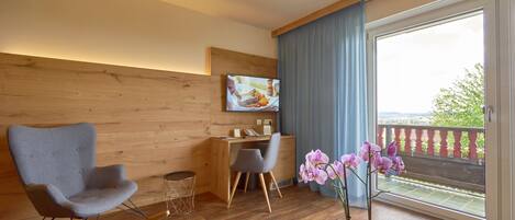 Une chambre moderne avec un mur en bois, un bureau, deux chaises, une télévision et un balcon avec vue.