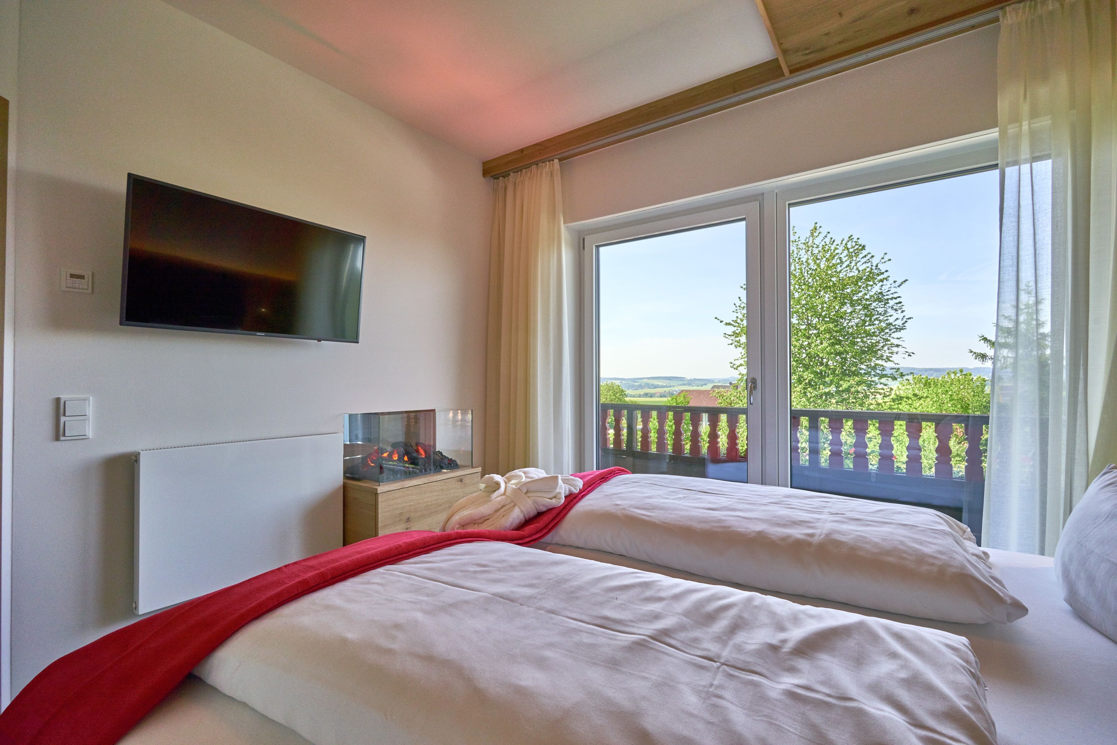 A hotel room with two beds, a TV mounted on the wall, and a view of the outdoors.