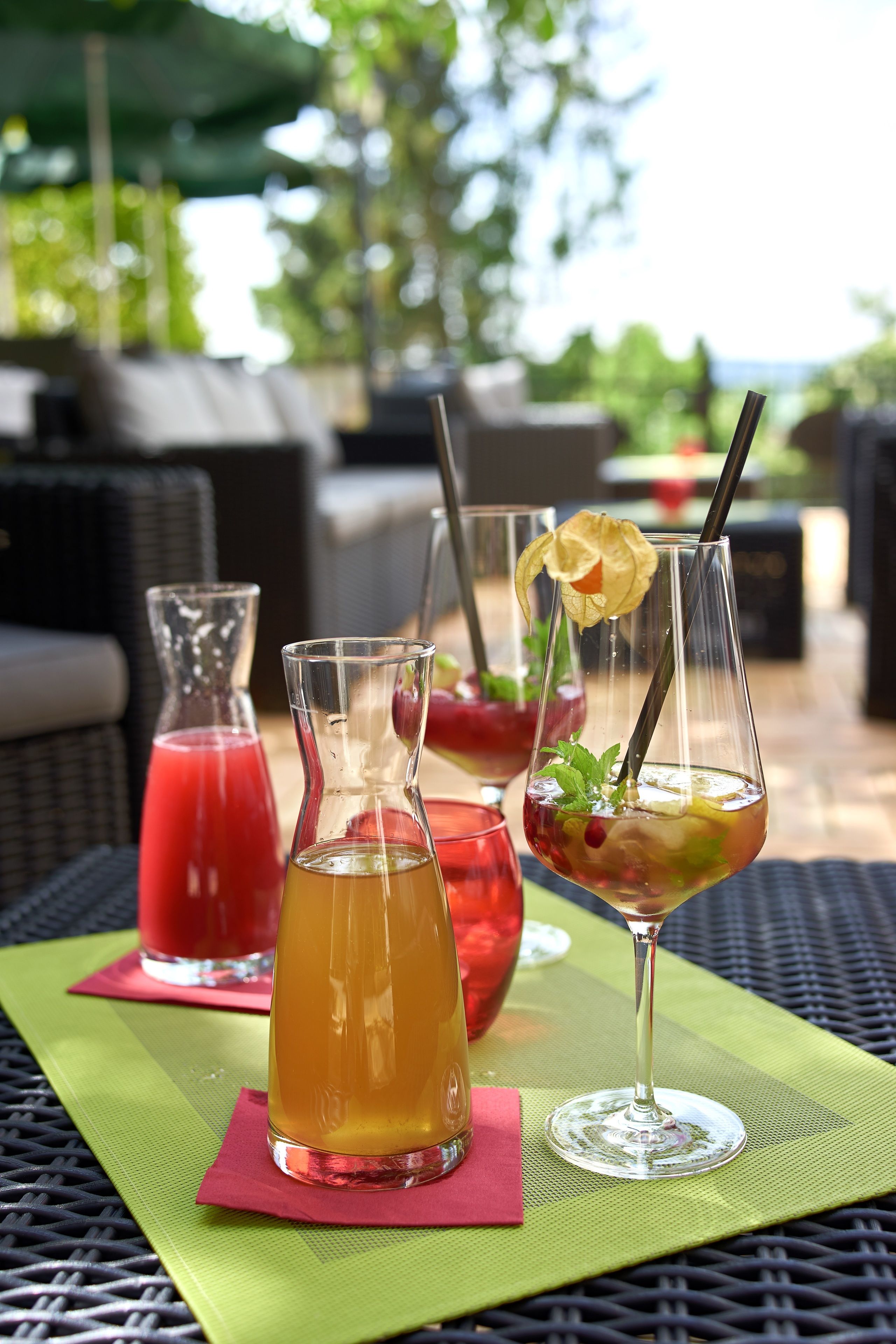 A table with three drinks on a green mat, a wicker chair, and a wicker sofa in the background.