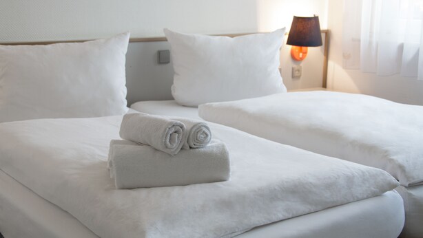 A hotel room with two beds, white linens, and a lamp on the nightstand. - Landgasthof Waldrast (Voehrenbach)
