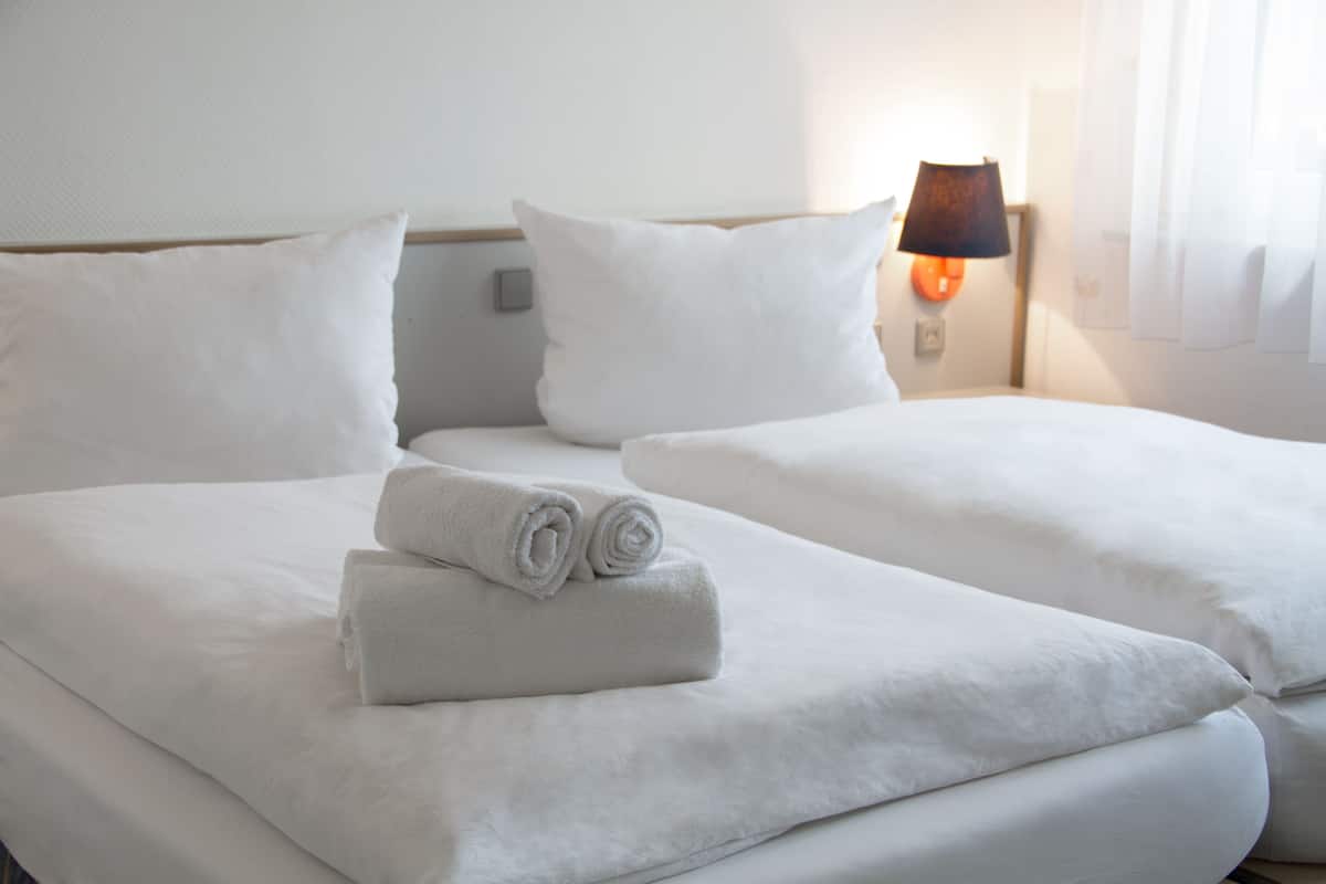 A hotel room with two beds, white linens, and a lamp on the nightstand.