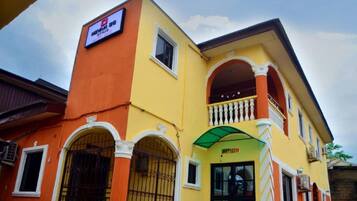 Un edificio de varios pisos con fachada amarilla y naranja, un balcón con balaustradas blancas y un letrero que indica un uso comercial o empresarial.