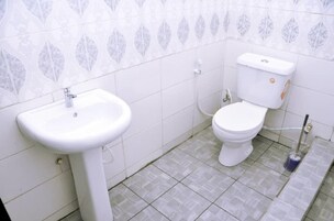 Un baño con lavamanos blanco, inodoro y suelo de baldosas.