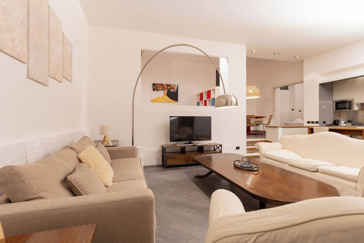 A modern living room with a sofa, coffee table, and TV. There is a kitchen area in the background.