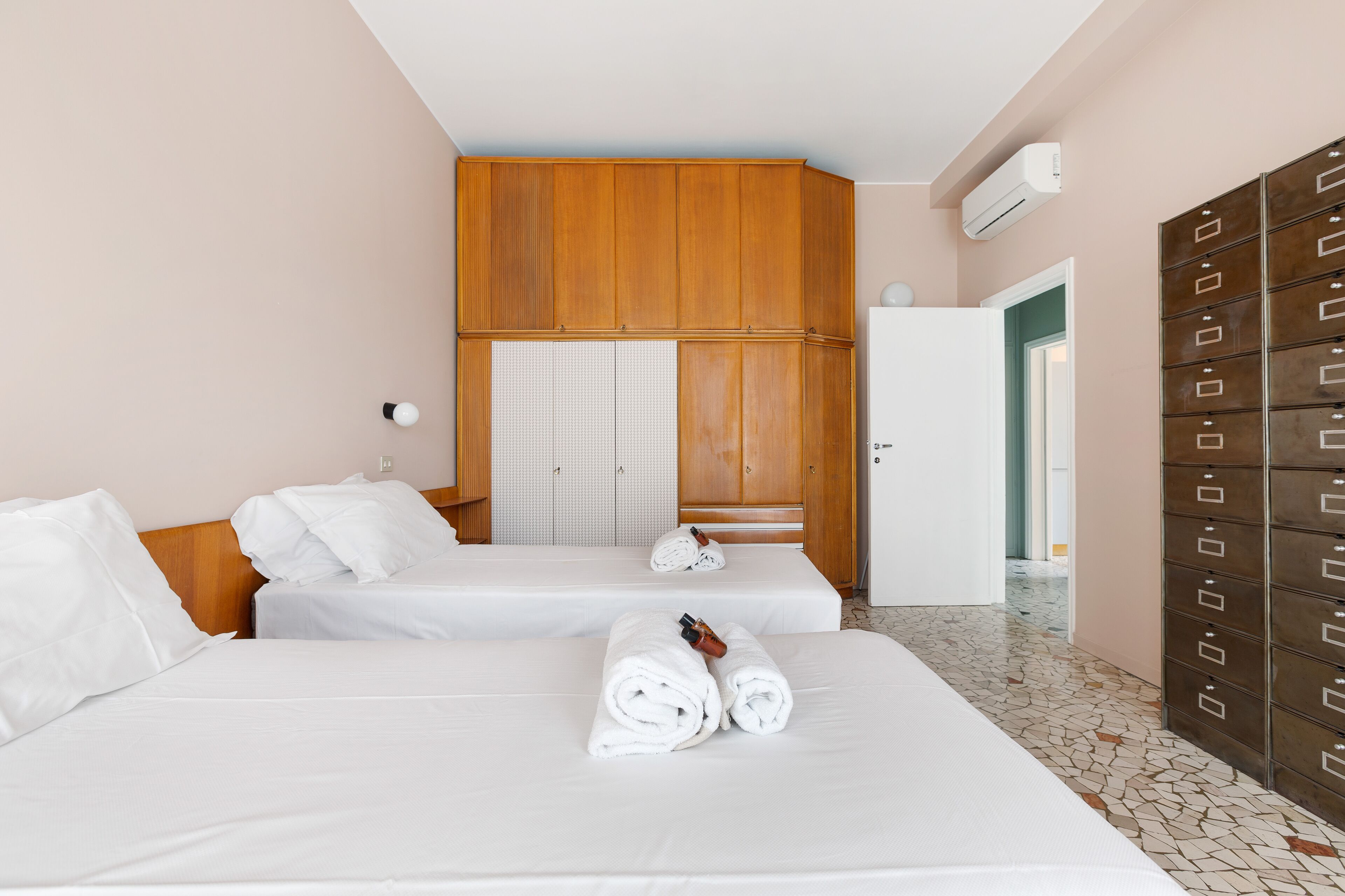 A hotel room with two beds, a wardrobe, and a tiled floor.