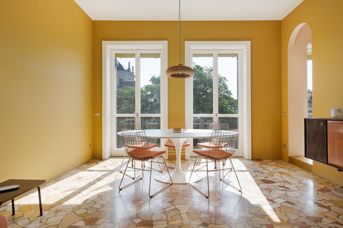 A dining area with a white table and chairs, large windows, and a tiled floor.