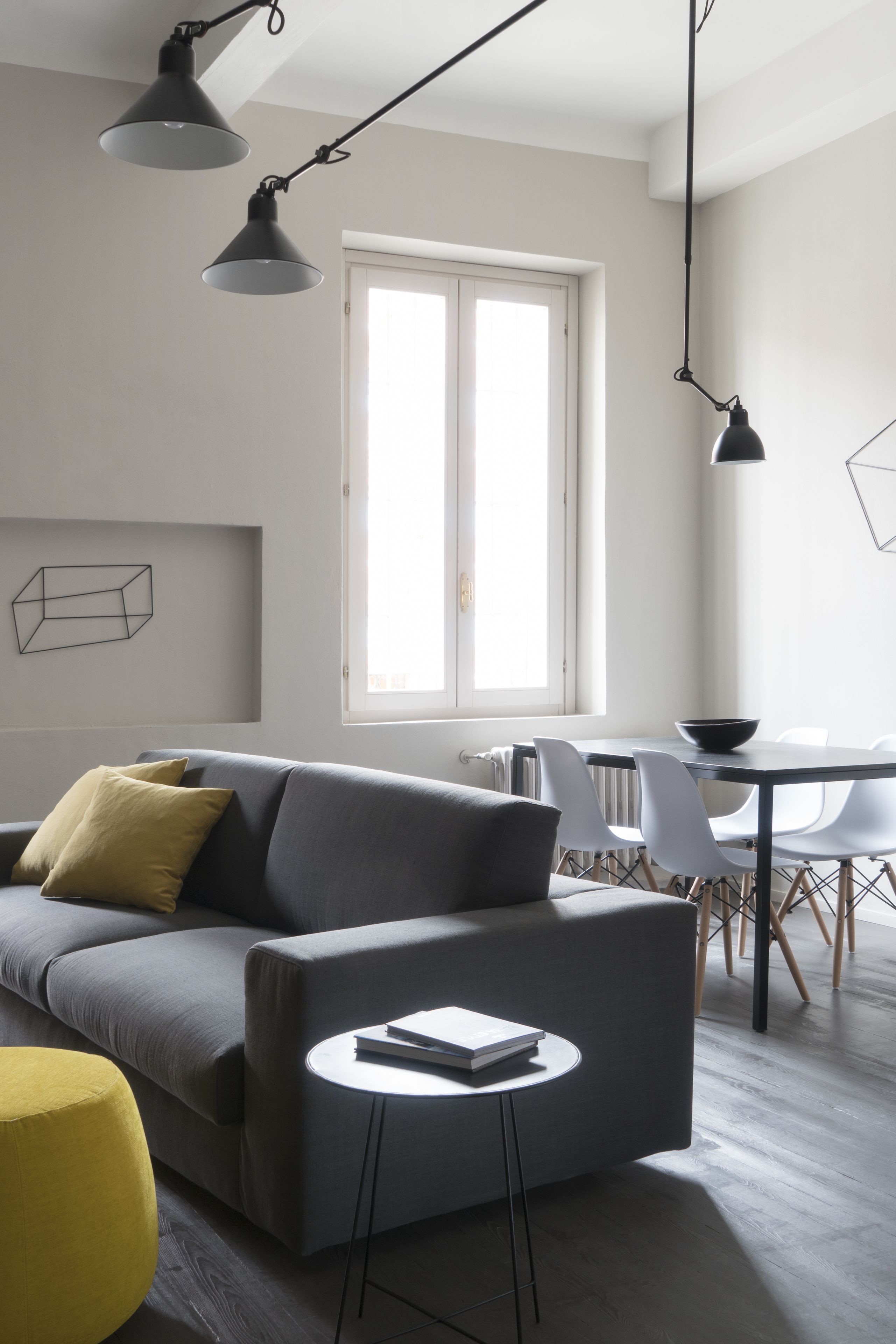 A modern living room with a gray sofa, a small round table, and a yellow ottoman. There is a dining area with a white table and chairs.