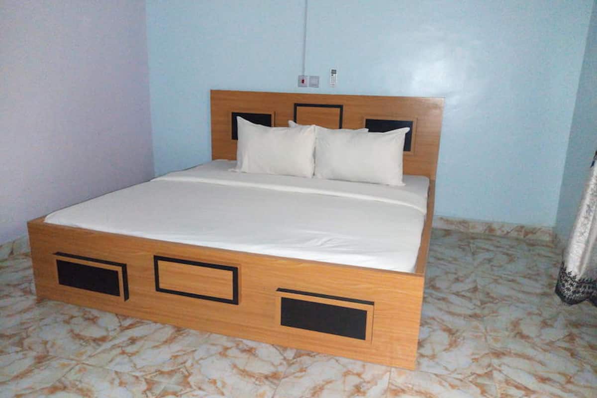 A bed with a wooden frame and a white mattress in a room with light blue walls and patterned floor tiles.