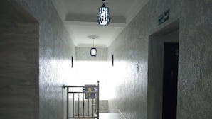 A hallway with a metal gate, a fire exit sign, and a ceiling light fixture. - De Maria Inn (Lagos)