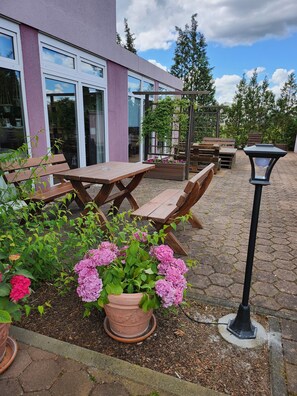 An outdoor patio with wooden tables and chairs, a potted plant with pink flowers, and a street lamp.